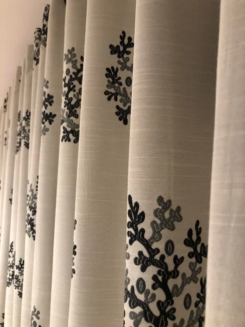 Pleated curtains in a pale linen-look fabric with a navy coral-branch pattern