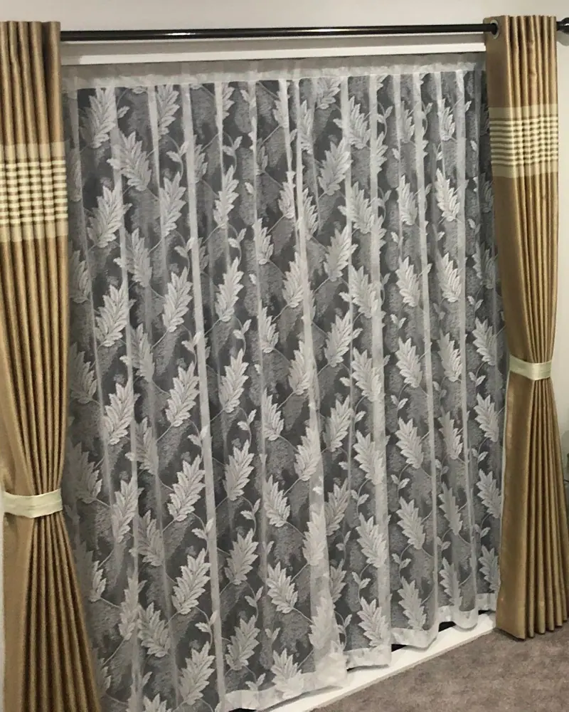 Leaf-pattern lace sheer framed by gold eyelet curtains with tiebacks