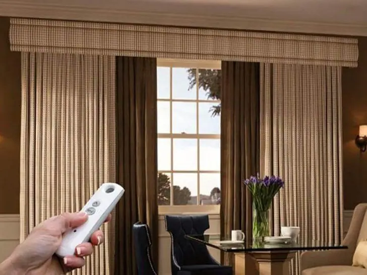 Hand holding a remote control in front of motorised curtains