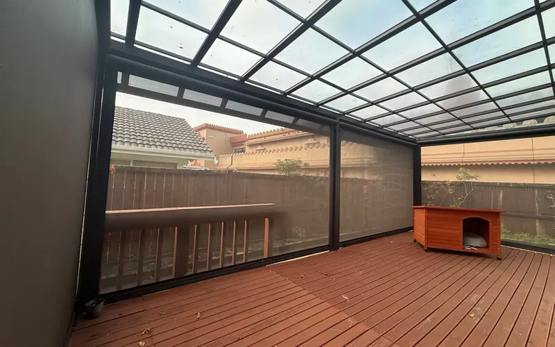Outdoor mesh blinds enclosing a deck under a glass-roofed pergola