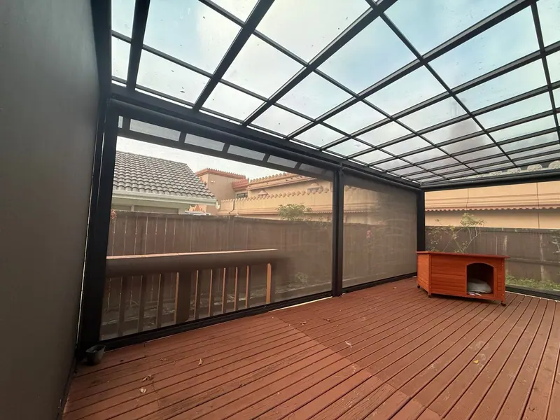 Outdoor mesh blinds enclosing a deck under a glass-roofed pergola