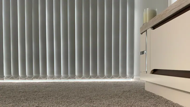 White vertical blinds filtering daylight in a carpeted room